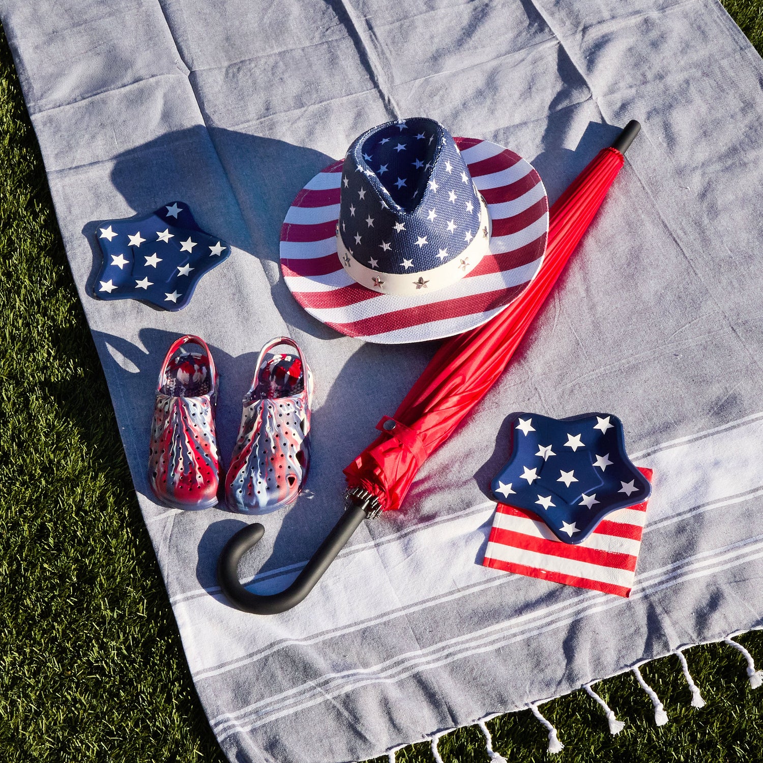 American flag-themed items including a hat, shoes, and umbrella on a gray blanket outdoors.