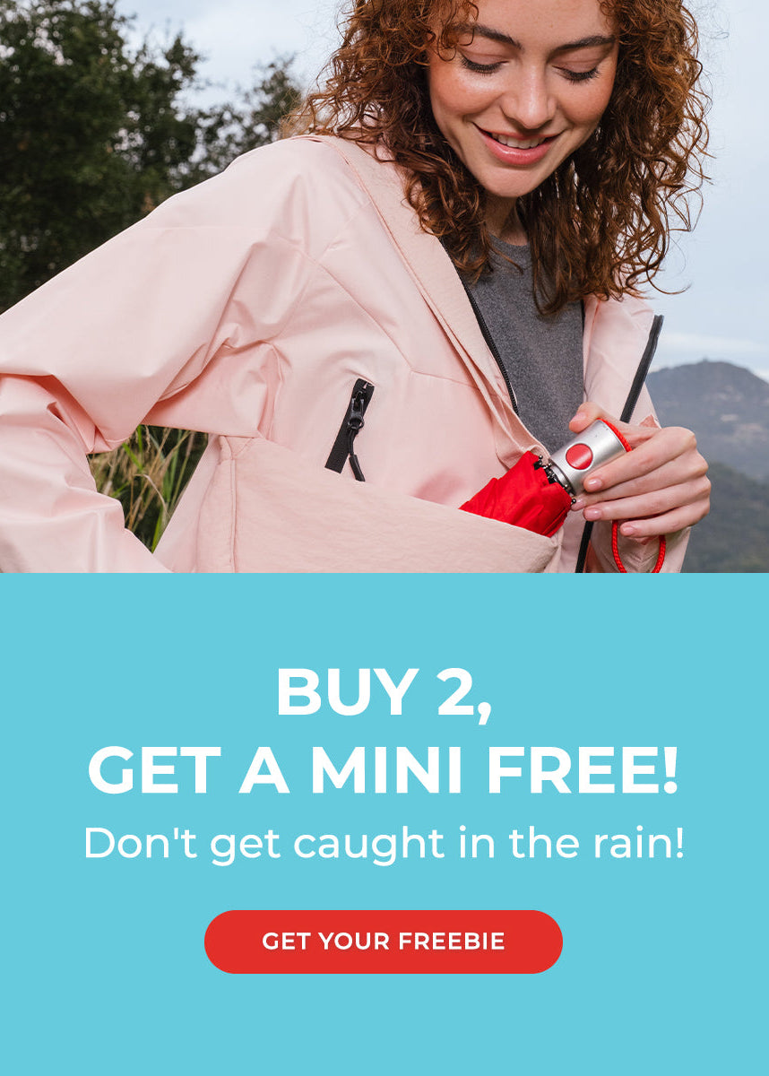 A promotional outdoor photo shows a woman wearing a light pink waterproof jacket and reaching into a red insulated bottle pouch. The lower half has a large turquoise text block reading 'BUY 2, GET A MINI FREE! Don't get caught in the rain!' with a red 'GET YOUR FREEBIE' button.