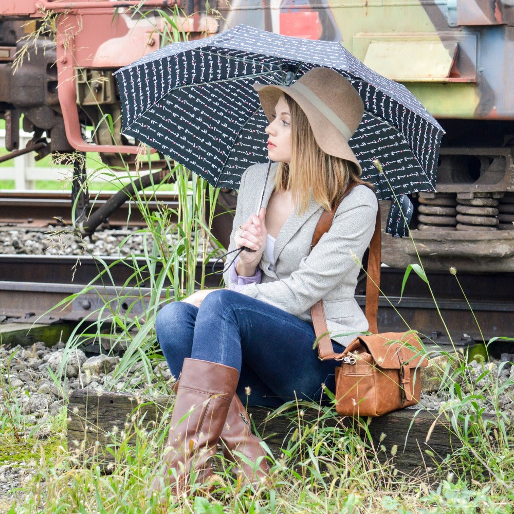 Woman holding Limited-Edition Auto Open Umbrella in love letter outside sitting on train tracks