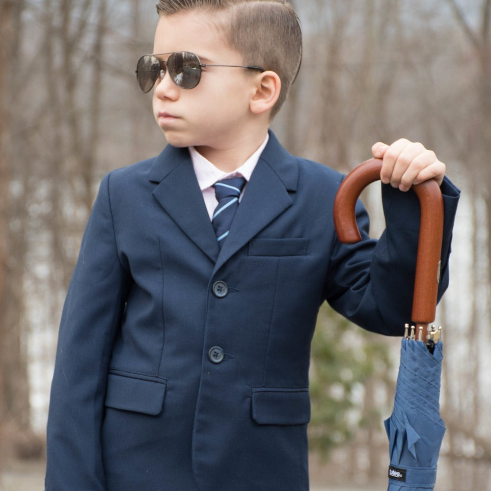 Little boy holding the Blue Line Auto Wooden Stick Umbrella wearing a tux and sunglasses outside frontal view