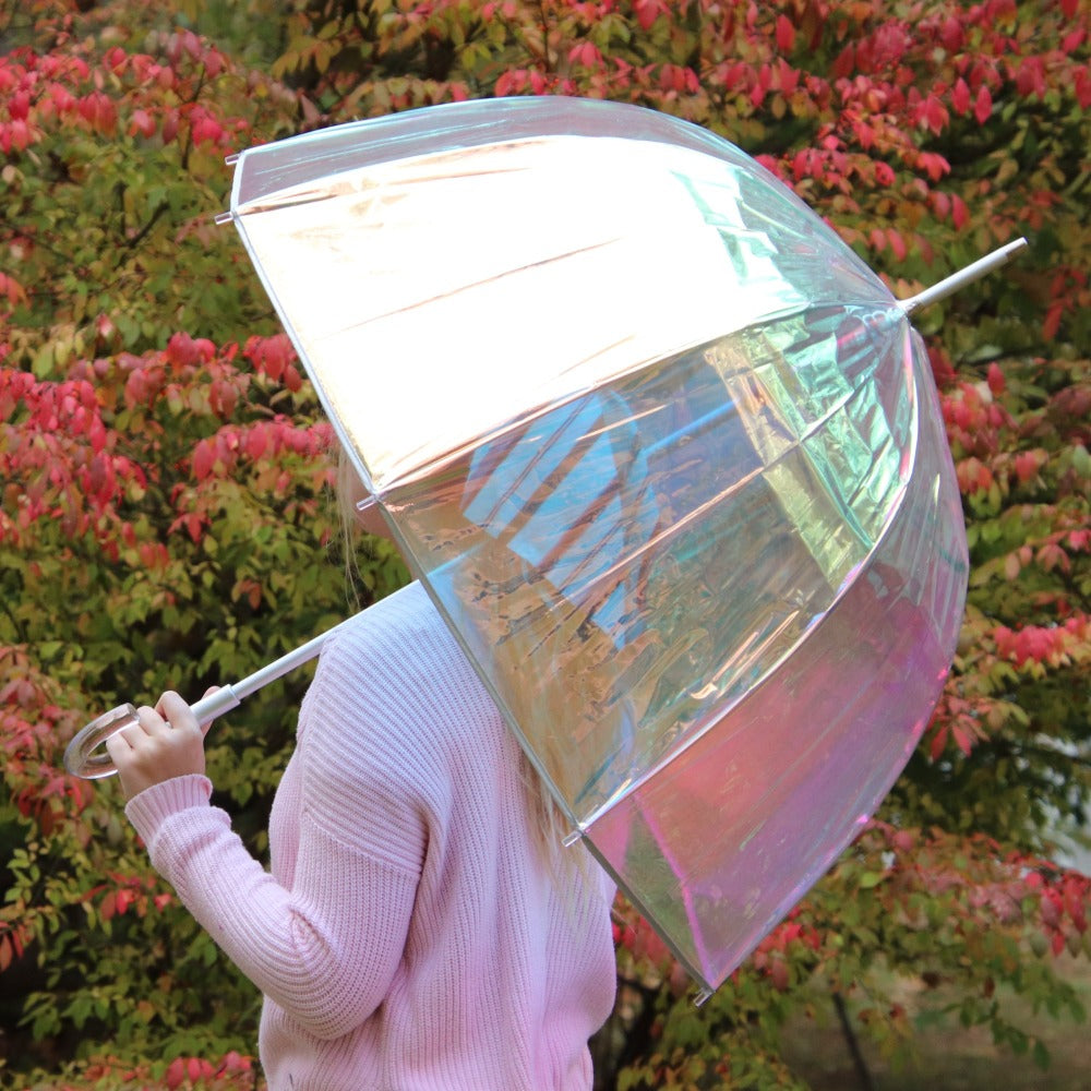 Woman holding Signature Clear Bubble Umbrella in Iridescent in front of fall colored leaves back side view
