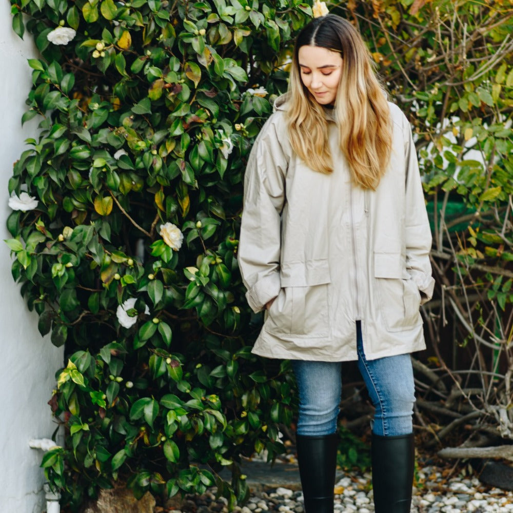 Lined Rain Slicker in Khaki on figure. Female Model standing in front of lush bushes wearing rain slicker and Cirrus boots