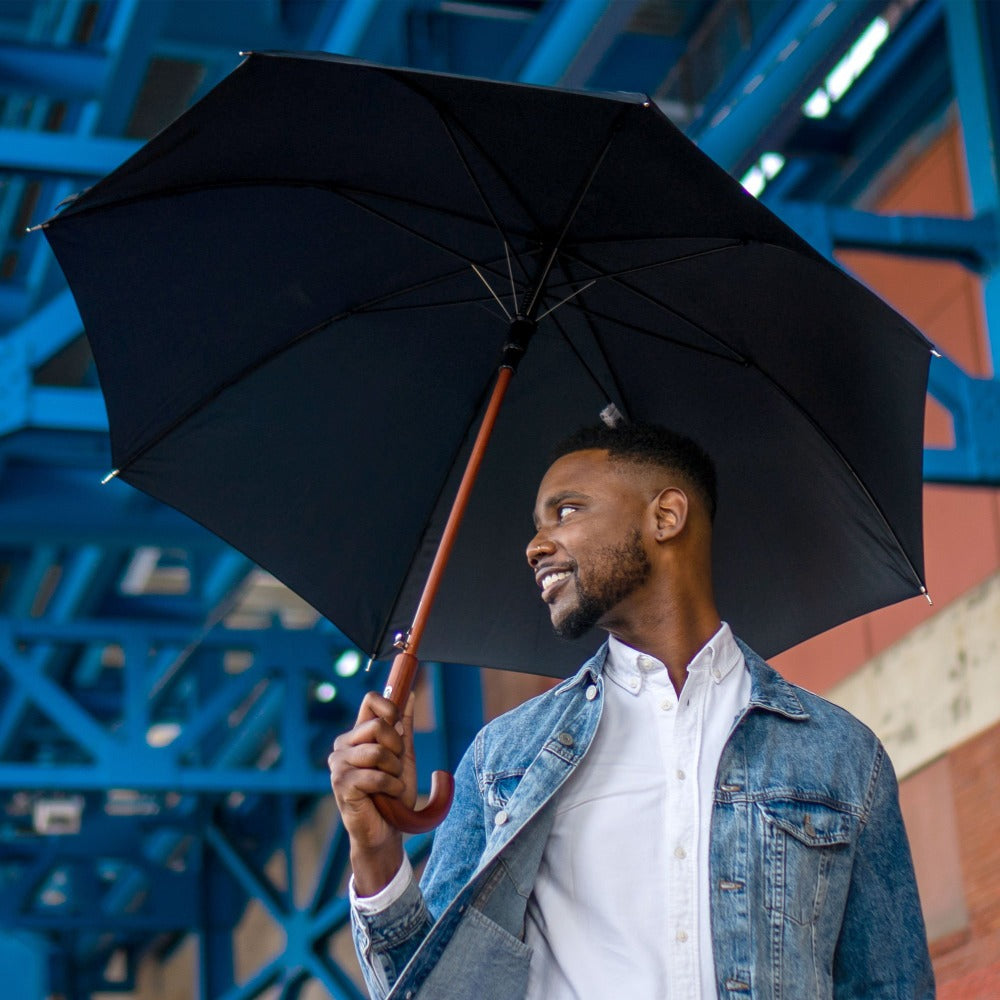 Male model holding black stick umbrella under city scaffolding 