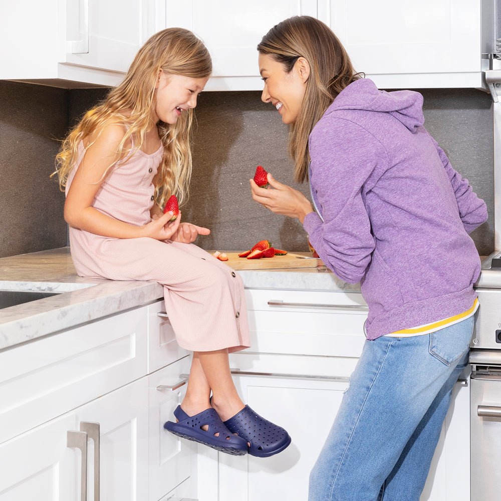 Mother and daughter eating strawberries. Little girl is sitting on the counter with her Splash and Play Navy  Blue Clogs